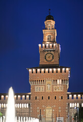 Castello Sforzesco (Sforza Castle) tower on Piazza Castello with fountain in front of Castello Sforzesco (Sforza Castle) in Milan, Italy, in the evening with dark blue sky