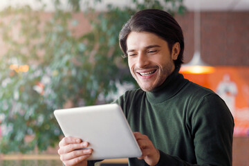 Application for business. Joyful businessman using digital tablet at modern cafe, drinking coffee, empty space