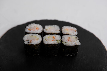 Close-up of six shrimp maki sushi rolls wrapped in nori, served on a black slate plate. Fresh and...