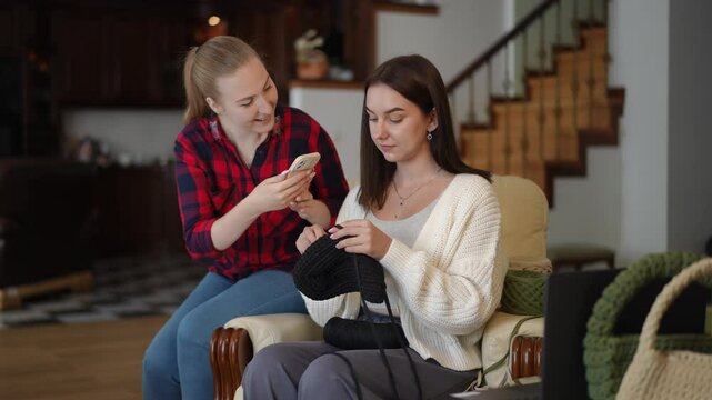 Two close friends find joy in indoor crafting activities as they share enjoyable moments on their smartphones