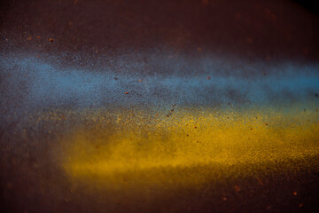 Close-up of a textured surface featuring blue and yellow spray paint blending together, creating an abstract and artistic effect with scattered particles. Ukraine flag