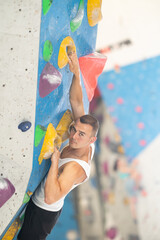 Active young man engaged in bouldering activity in rock climbing hangar