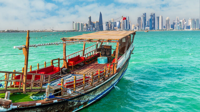 Traditional arab dhow fishermen boat with qatari flag at the sea bay with Doha modern business downtown center skyline, Qatar