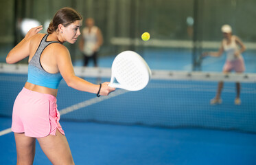 Young female tennis player plays against adult woman and young guy on tennis court