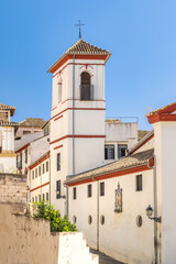 Fototapeta premium Granada town in Spain. Whitewashed building with red trim and bell tower against a vibrant blue sky. A charming architectural detail in a sunny, historical setting.