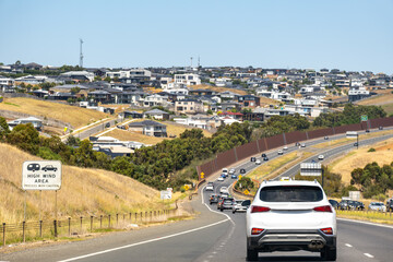 A multi-lane, busy highway or main road with many cars, alongside a hillside residential development near Geelong, Australia, with many houses. concept of a new estate, suburban expansion