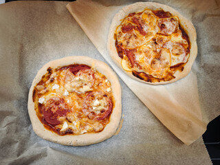 Two mini pizzas baking on parchment paper with tomato and cheese