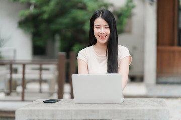 Tech-Savvy and Smiling: A young woman beams with joy, engrossed in her laptop amidst a natural,...