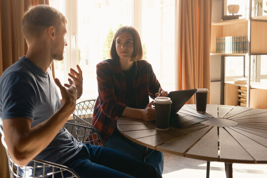 Two individuals engaged in discussion while seated at a table with coffee cups.
