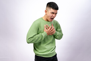An Asian man in a green sweatshirt clutches his chest with both hands, his face showing discomfort...