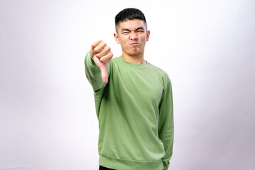 An Asian man in a green sweatshirt stands against a white background, making a thumbs-down gesture...