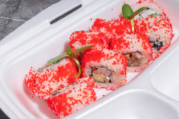 A set of sushi rolls with red tobiko topping, neatly arranged in a styrofoam container.