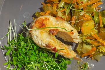 Close-up of a perfectly cooked fish fillet with a crispy crust, served with vegetables and microgreens.