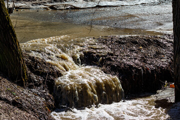A stream of dirty water flowing off the road during snowmelt in spring