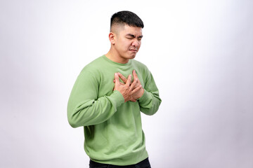An Asian man in a green sweatshirt clutches his chest with both hands, his face showing discomfort...