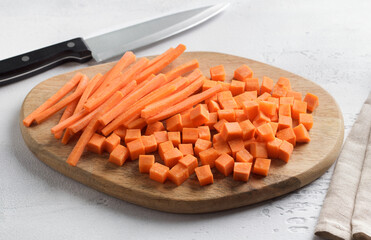 Cubes and sticks of fresh ripe carrots on a wooden board, two types of cutting vegetables. Healthy diet food