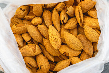 A close-up of almonds in various stages of being cracked open, showing the shells and nuts inside,...