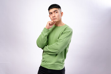 An Asian man in a green sweatshirt poses with a thoughtful expression, resting his chin on his hand...
