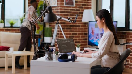 Software developer types programming code in a cozy home office setup. Asian woman coding for cloud...