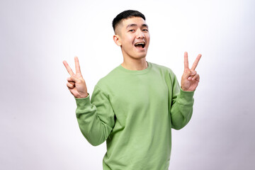 An Asian man in a green sweatshirt is making a peace sign with his right hand while slightly...