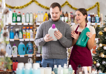 Young woman seller offers laundry detergent to young man buyer in household chemicals store...