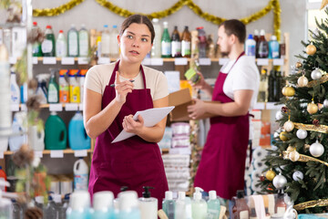 Female salesperson makes notes on paper - keeps track of goods. Male salesperson puts goods on shelves, in the background