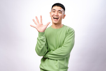 An Asian man in a green sweatshirt is smiling while holding up five fingers on his right hand. His left arm is crossed, and he stands against a white background, conveying a friendly