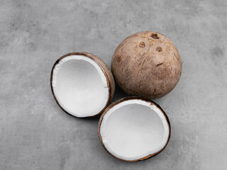Whole and two halves of coconut resting on gray surface. Copy space, banner