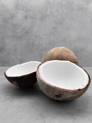 Two halves of fresh coconut resting on gray surface with whole coconut behind. Copy space, banner