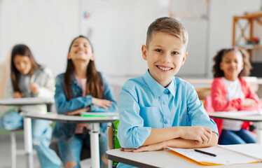 Fototapeta premium Smart schoolchildren sitting at school desks, focus on smiling boy with diverse classmates on background. Education concept