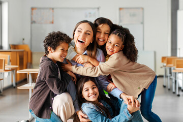 Friendly atmosphere in the classroom, happy diverse kids embracing female teacher appreciating and...