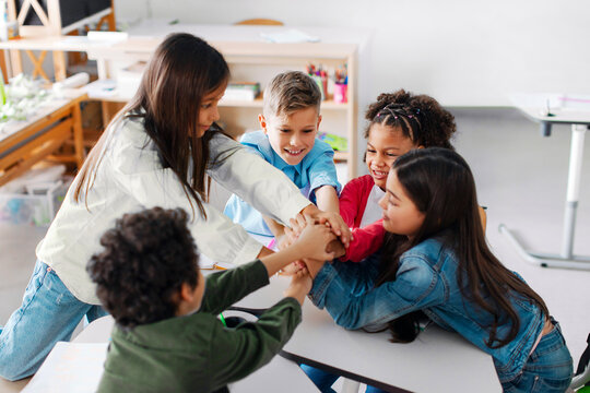 Team of diverse school children joining hands, sitting in circle in classroom, having bonding moment, feeling united and supported