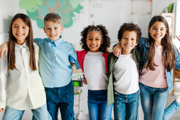 Group of happy diverse school friends embracing and smiling at camera, posing in classroom at the...