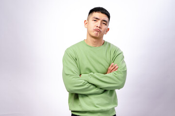 An Asian man wearing a green sweatshirt stands against a white background with his arms crossed and...