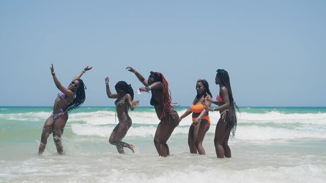 Group of joyful women playing and dancing on a sandy beach during a summer day enjoying vacation on the beach together, slow motion
