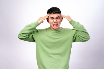 An Asian man wearing a green sweatshirt against a white background is pressing his temples with...