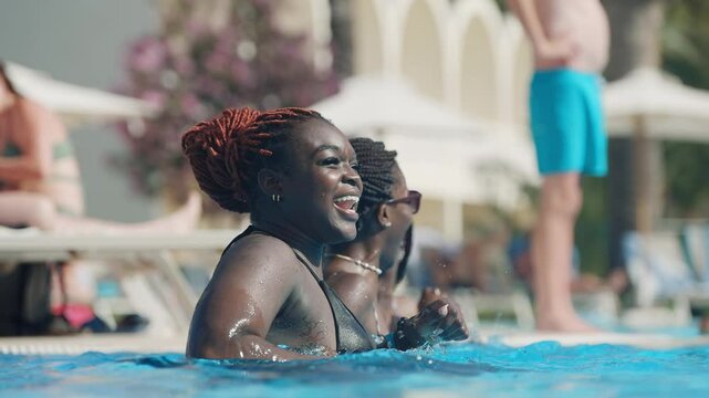 Happy smiling black women enjoying a fun day at a sunny outdoor swimming pool dancing in slow motion
