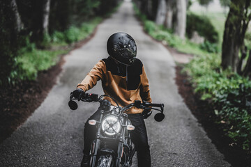 Hombre adulto en motocicleta negra por camino rodeado de arboles en día lluvioso