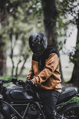 Hombre adulto en motocicleta negra por camino rodeado de arboles en día lluvioso