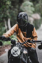 Hombre adulto en motocicleta negra por camino rodeado de arboles en día lluvioso