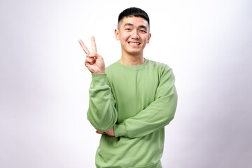 An Asian man in a green sweatshirt is making a peace sign with his right hand while slightly...