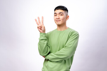An Asian man in a green sweatshirt is smiling while holding up three fingers on his right hand. His...