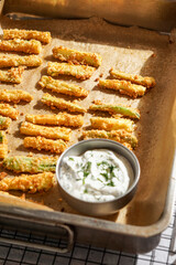 Healthy crunchy zucchini nuggets with sauce, on a grey stone background with bright sunlight, and a glass of white wine