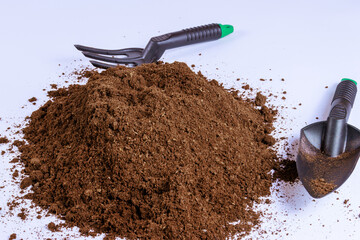 Pile of peat on white background with garden tools. Compost for sowing vegetable seeds.