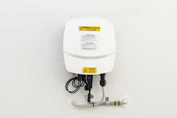 Solar inverter equipment attached to a white wall with cables connections warning lables and green lights showing energy produced