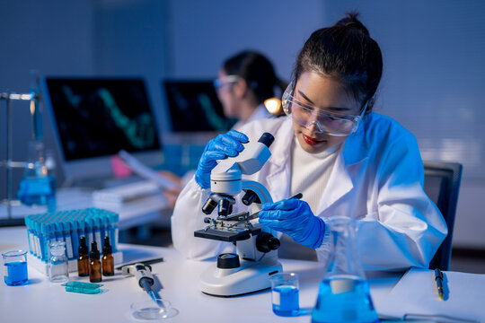 A woman in a lab coat is looking through a microscope