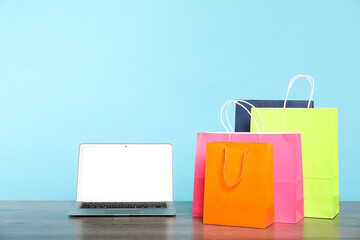 Internet shopping. Laptop and colorful paper bags on wooden table against light blue background