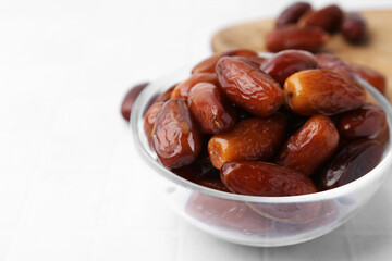 Tasty dried dates in glass bowl on white table, closeup. Space for text