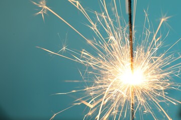 Bright burning sparkler on light blue background, closeup