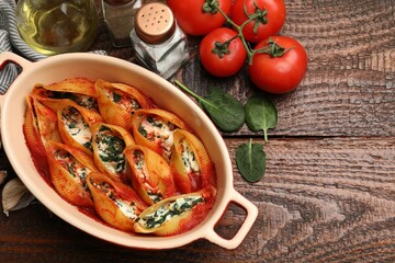 Delicious conchiglie pasta with ricotta cheese, spinach and tomato sauce in baking dish on wooden table, flat lay. Space for text